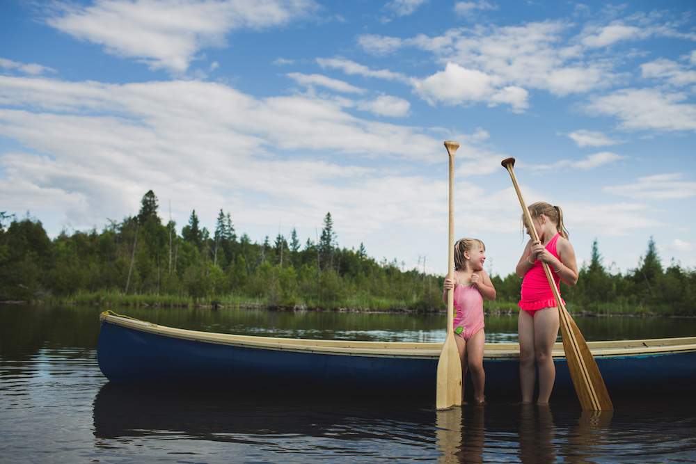 Two young sisters chatting next to canoe on Indian river, Ontario, Canada